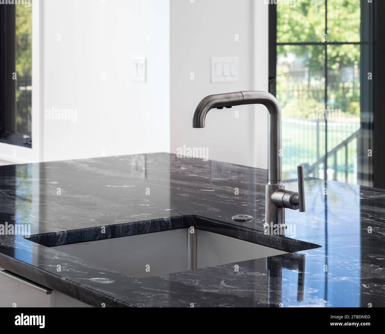 Una moderna cucina con rubinetti in acciaio inossidabile nero su un'isola con un ripiano in marmo nero, finestre con cornice nera e pareti bianche. Foto Stock