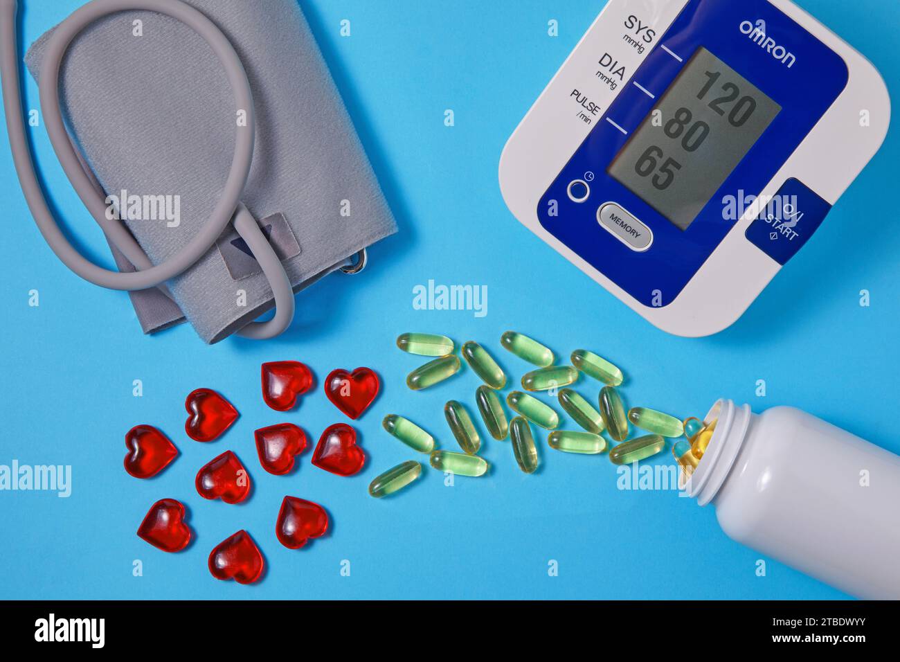 Gli acidi grassi polinsaturi Omega-3 e i cuori rossi fuoriescono da una vaschetta di plastica bianca e da un misuratore della pressione sanguigna su sfondo blu. Prevenzione e. Foto Stock