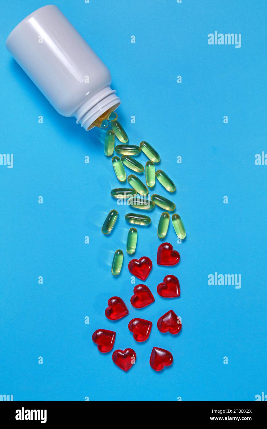 Gli acidi grassi polinsaturi Omega-3 e i cuori rossi fuoriescono da un vaso di plastica bianco su sfondo blu. Prevenzione e trattamento dell'aterosclerosi Foto Stock