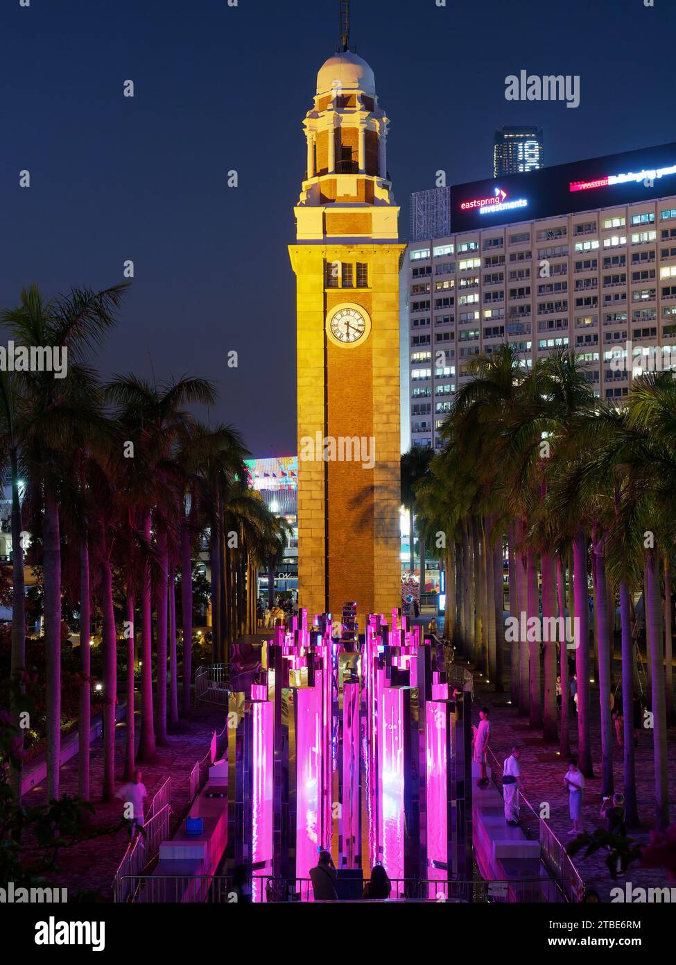 Guardando la vecchia torre dell'orologio della stazione ferroviaria di Kowloon a Hong Kong di notte con un'esposizione di luci colorate Foto Stock