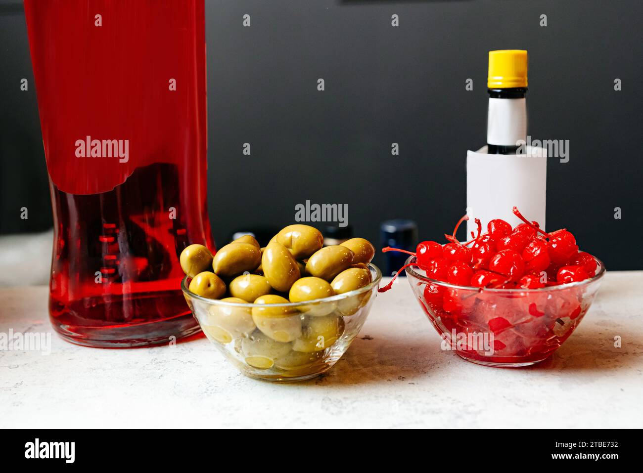 Olive verdi e ciliegie al maraschino esposte con una bottiglia di alcol rosso su un bancone del bar Foto Stock
