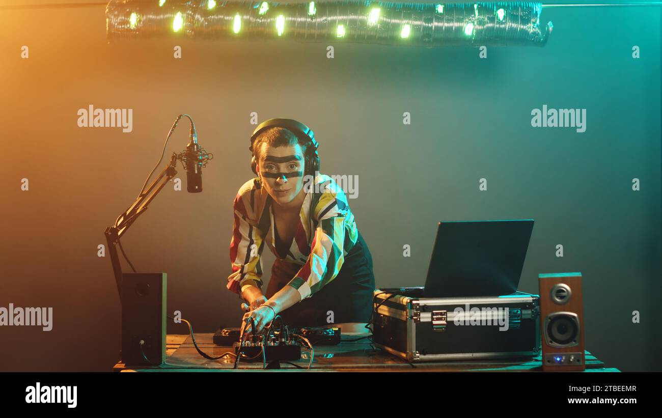 Artista femminile che mixa canzoni techno sui pulsanti audio, divertendosi con i giradischi che suonano musica moderna alle feste in nightclub. Tasto di controllo dei bassi per i giovani esecutori, regolazione del volume. Scatto con treppiede. Foto Stock