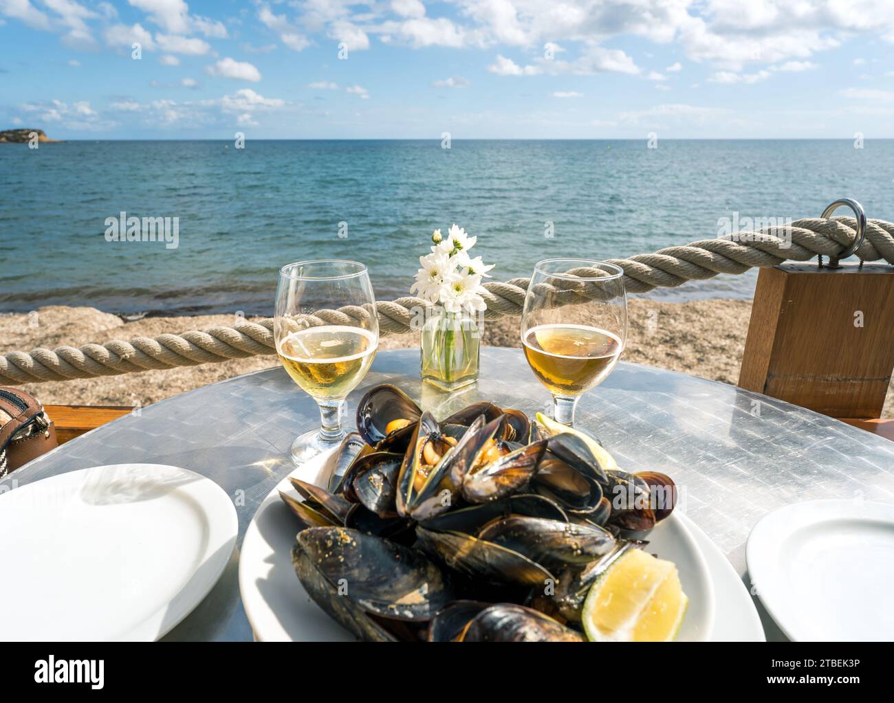 Indulgenza sulla spiaggia: Un piatto di cozze fresche e due bicchieri di vino creano un ambiente idilliaco sul mare, dove il sapore incontra la serenità dell'oceano Foto Stock