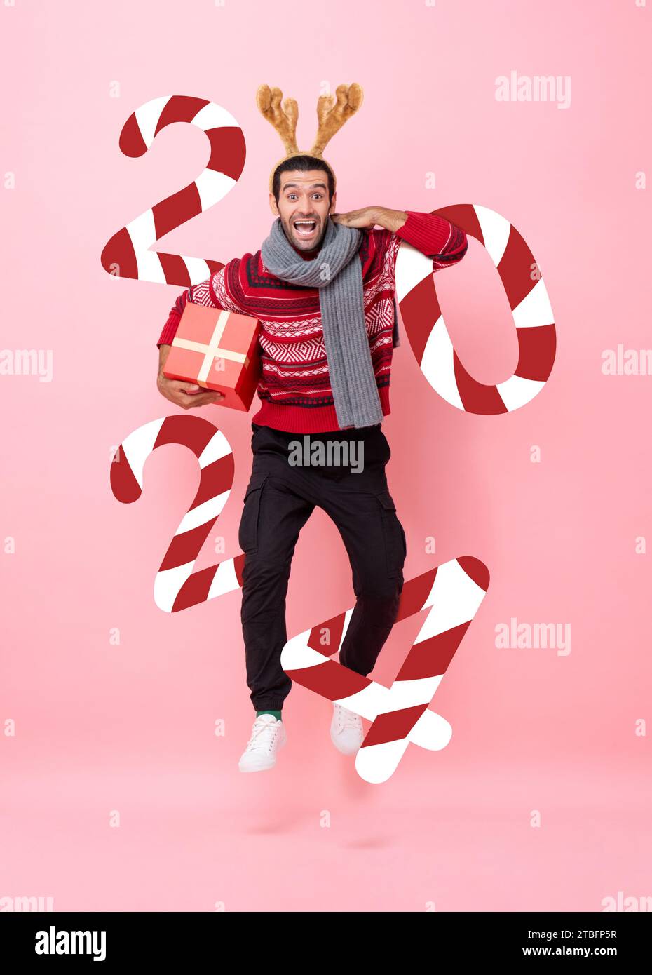 Divertente e gioioso uomo che indossa un abbigliamento natalizio con una confezione regalo con numero di Capodanno 2024 in colore rosa, sfondo isolato, ripresa in studio Foto Stock