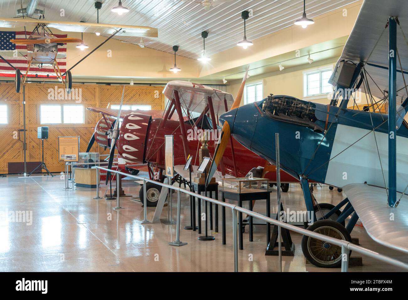 Un biplano blu e bianco con motore radiale si staglia a destra mentre una fila di biplani a strisce rosse si allontana lungo la sala del museo in Ohio. Foto Stock