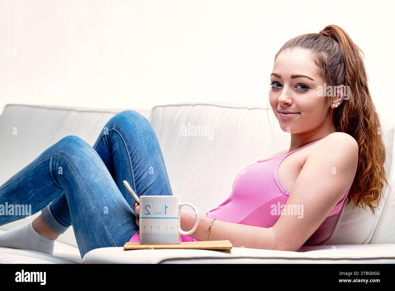 La posa casual della donna sul divano, i jeans blu abbinati a un top rosa, racchiudono una perfetta giornata di relax Foto Stock