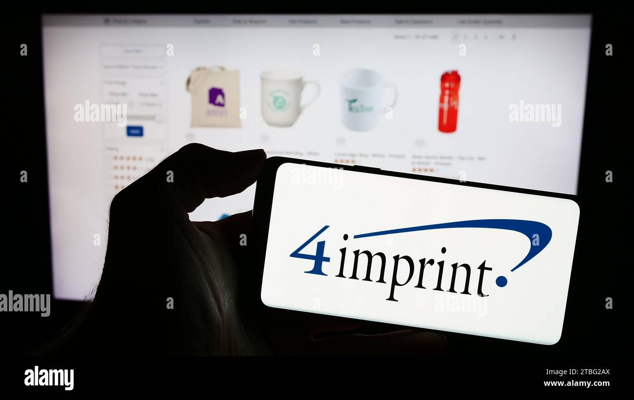 Persona che possiede uno smartphone con il logo della società di merchandising promozionale 4imprint Group plc davanti al sito Web. Concentrarsi sul display del telefono. Foto Stock