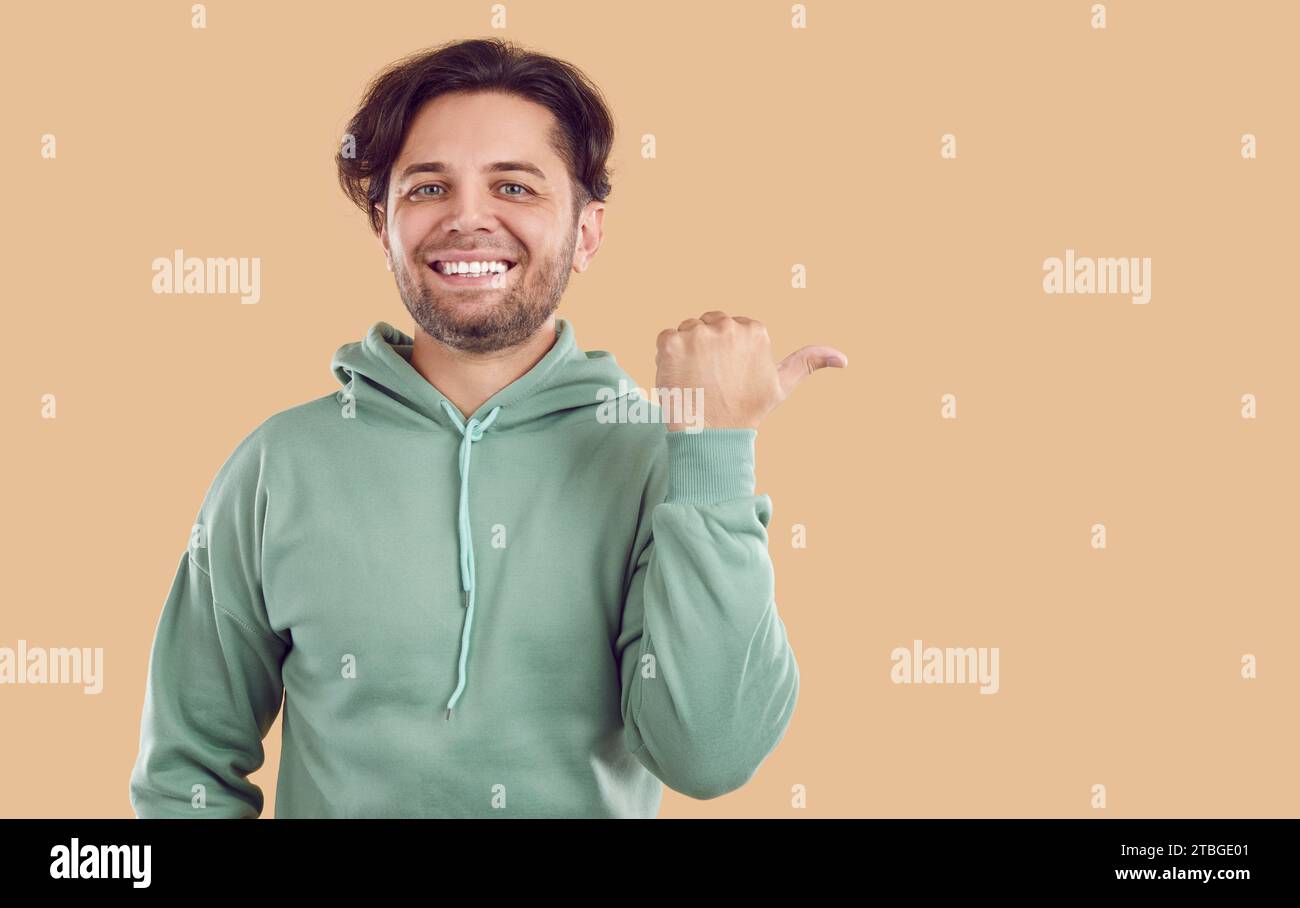 Striscione con un simpatico uomo sorridente in felpa verde che punta sullo spazio per la copia su sfondo beige. Foto Stock