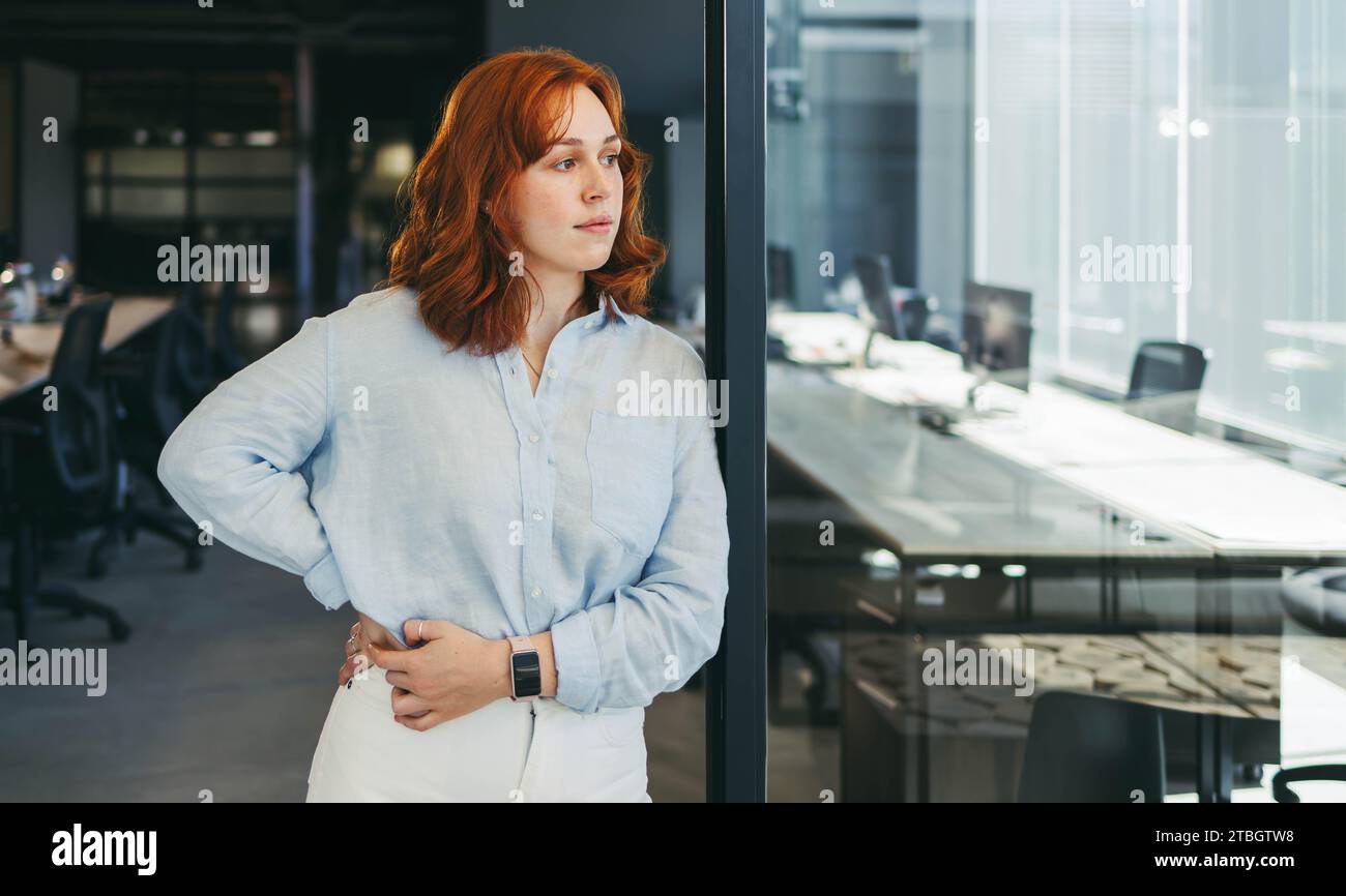 una donna d'affari si trova in un ufficio affollato e guarda con attenzione. È un'impiegata professionale, un'imprenditrice penosa in un'azienda tecnologica. Con la sua g Foto Stock