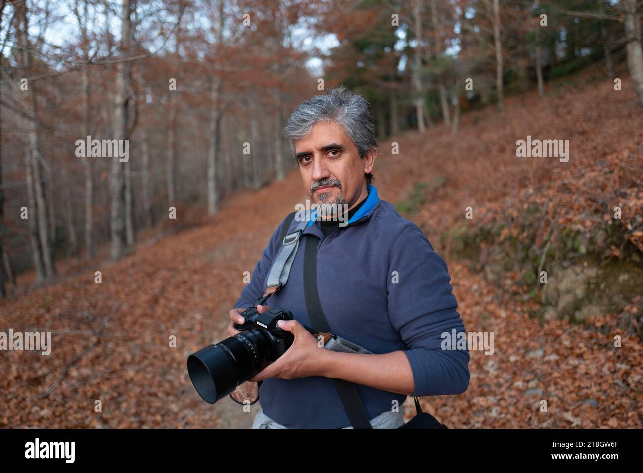 Ritratto a profondità di campo ridotta di un fotografo di paesaggi di mezza età che tiene la fotocamera mentre si trova in una foresta Foto Stock