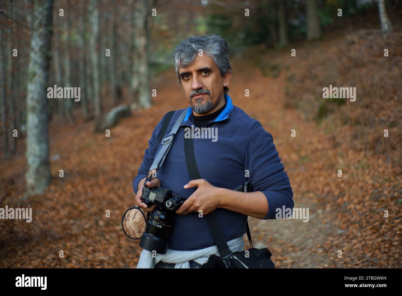 Ritratto a profondità di campo ridotta di un fotografo di paesaggi di mezza età che tiene la fotocamera mentre si trova in una foresta Foto Stock