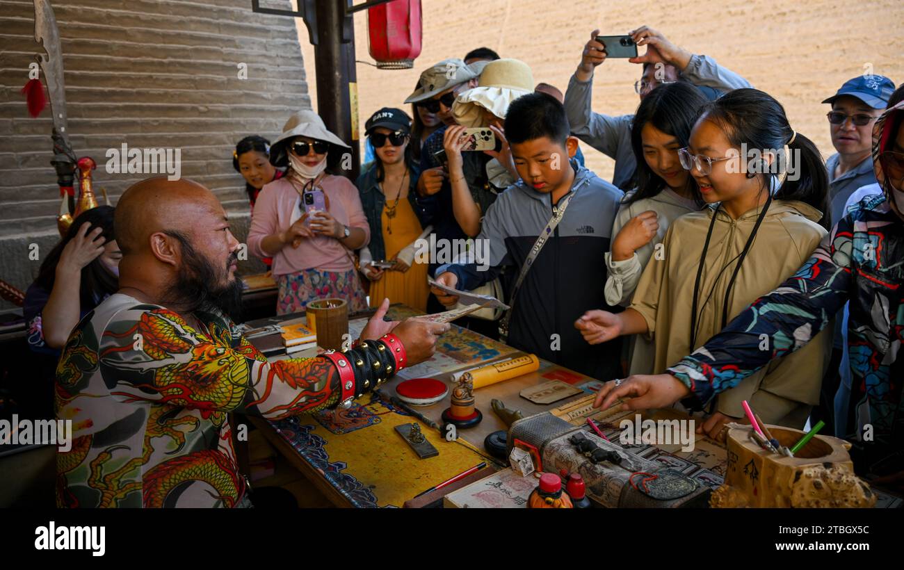 (231207) -- JIAYUGUAN, 7 dicembre 2023 (Xinhua) -- i visitatori acquistano antichi "visti" presso lo stallo di li Sen nell'area panoramica del passo Jiayu nella città di Jiayuguan, provincia del Gansu della Cina nord-occidentale, 14 luglio 2023. Li Sen, 43 anni, si guadagna da vivere interpretando il ruolo di un antico "generale" nell'area panoramica del passo Jiayu nella città di Jiayuguan, nella provincia del Gansu della Cina nord-occidentale. I visitatori possono acquistare antichi "visti" presso la sua bancarella. Questi documenti sono progettati da li e costituiscono una parte essenziale del gioco di ruolo, consentendo ai turisti di tornare nell'antica Cina. Guardando al futuro, li prevede di organizzare sistematicamente il Foto Stock