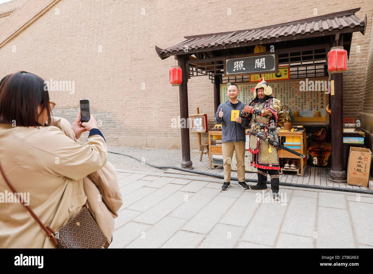 (231207) -- JIAYUGUAN, 7 dicembre 2023 (Xinhua) -- li Sen (R) posa per una foto con un visitatore nell'area panoramica del passo Jiayu nella città di Jiayuguan, provincia del Gansu della Cina nord-occidentale, 26 settembre 2023. Li Sen, 43 anni, si guadagna da vivere interpretando il ruolo di un antico "generale" nell'area panoramica del passo Jiayu nella città di Jiayuguan, nella provincia del Gansu della Cina nord-occidentale. I visitatori possono acquistare antichi "visti" presso la sua bancarella. Questi documenti sono progettati da li e costituiscono una parte essenziale del gioco di ruolo, consentendo ai turisti di tornare nell'antica Cina. Guardando al futuro, li prevede di organizzare sistematicamente il hi Foto Stock