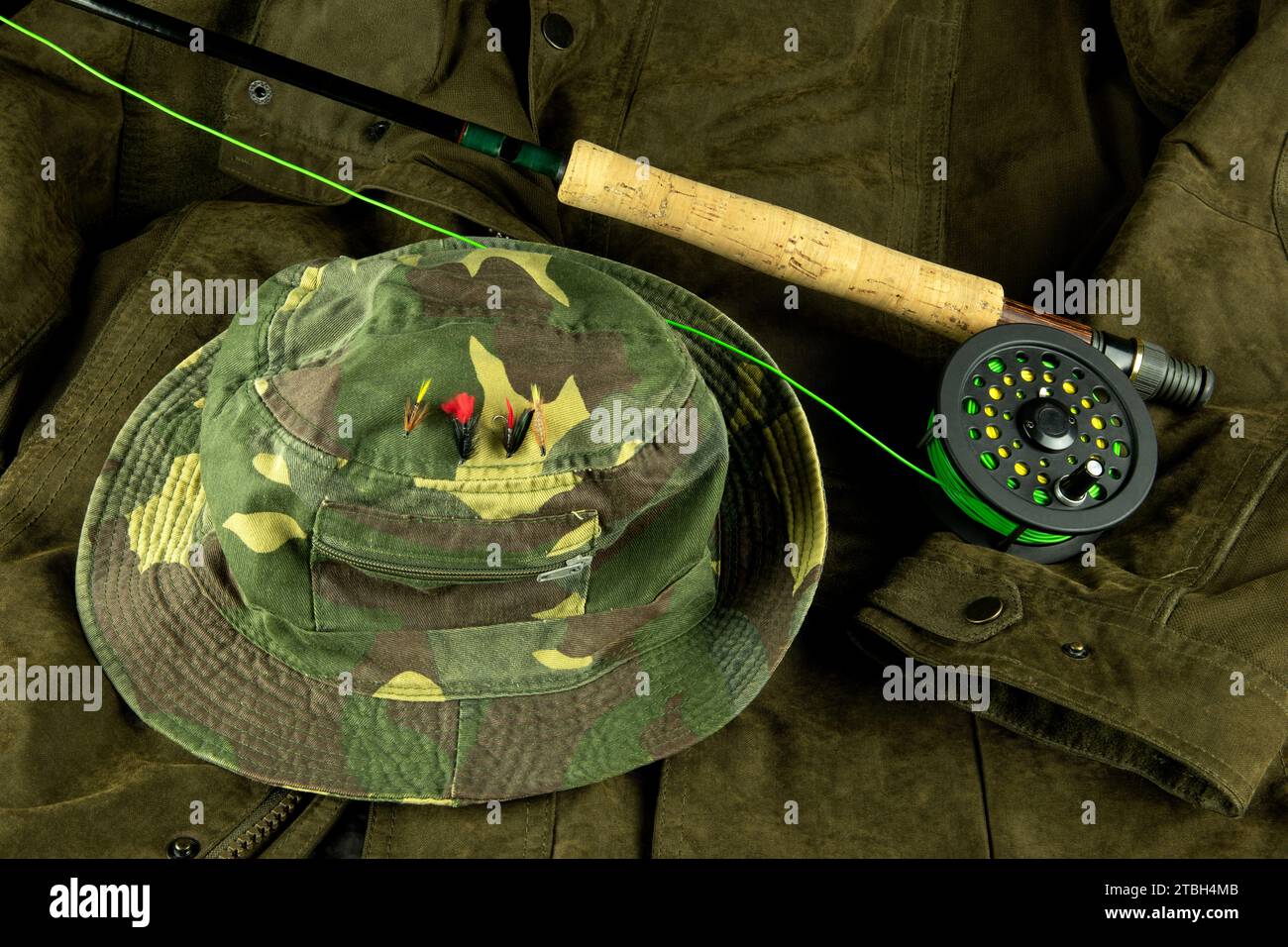 Canna da pesca con mosca e mulinello con lenza su un cappotto da esterno con mosche di trota su un cappello da pesca Foto Stock