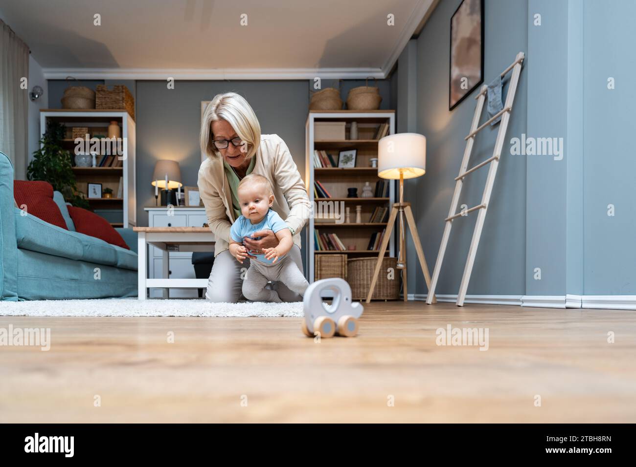 Nonna che si prende cura di suo nipote mentre i suoi genitori lavorano. La donna anziana lavora come tata, gioca con il bambino piccolo sul pavimento della casa. G Foto Stock