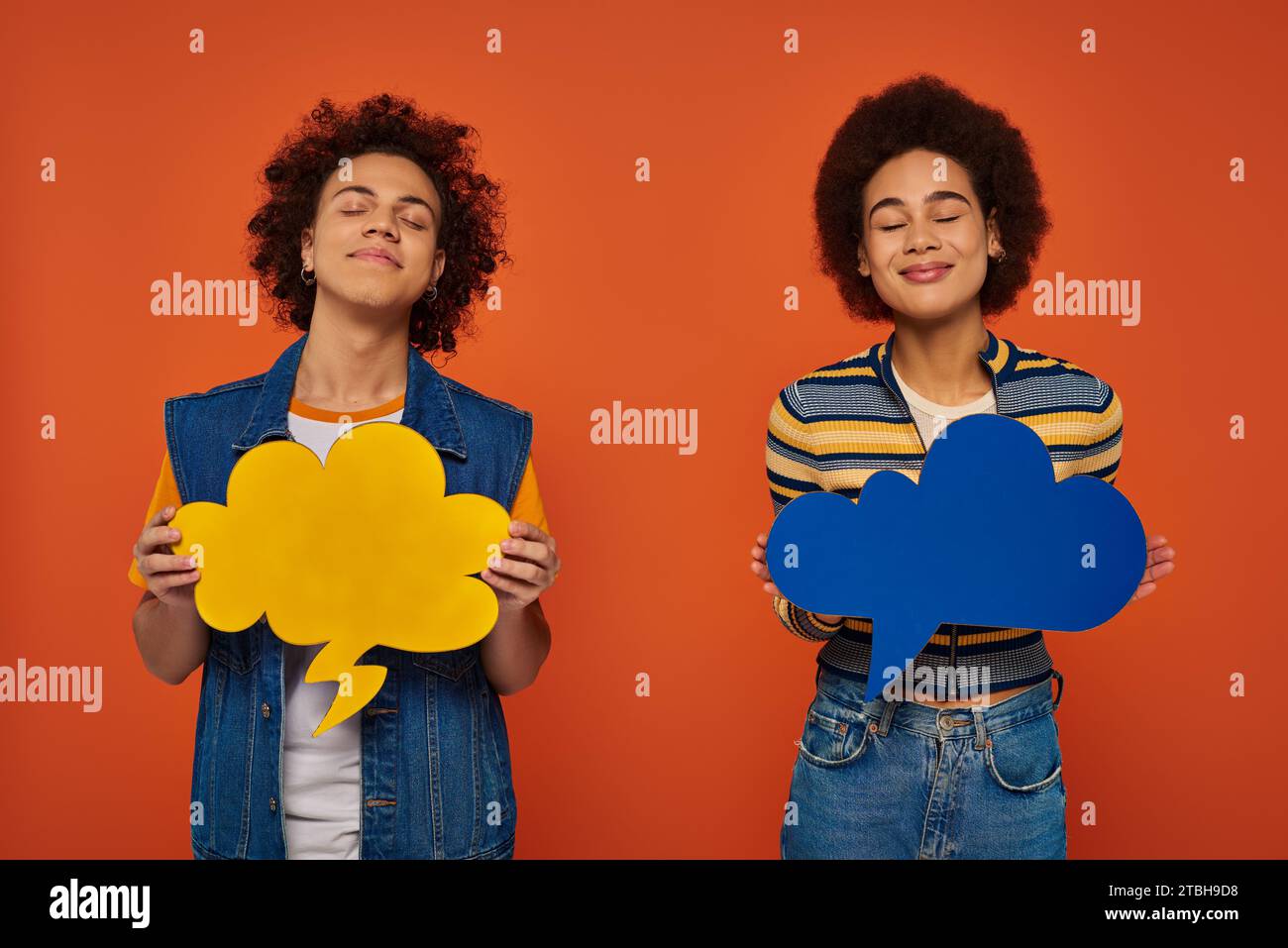 fratello e sorella afro-americani dall'aspetto gradevole che si mettono in posa con bolle di pensiero sullo sfondo arancione Foto Stock