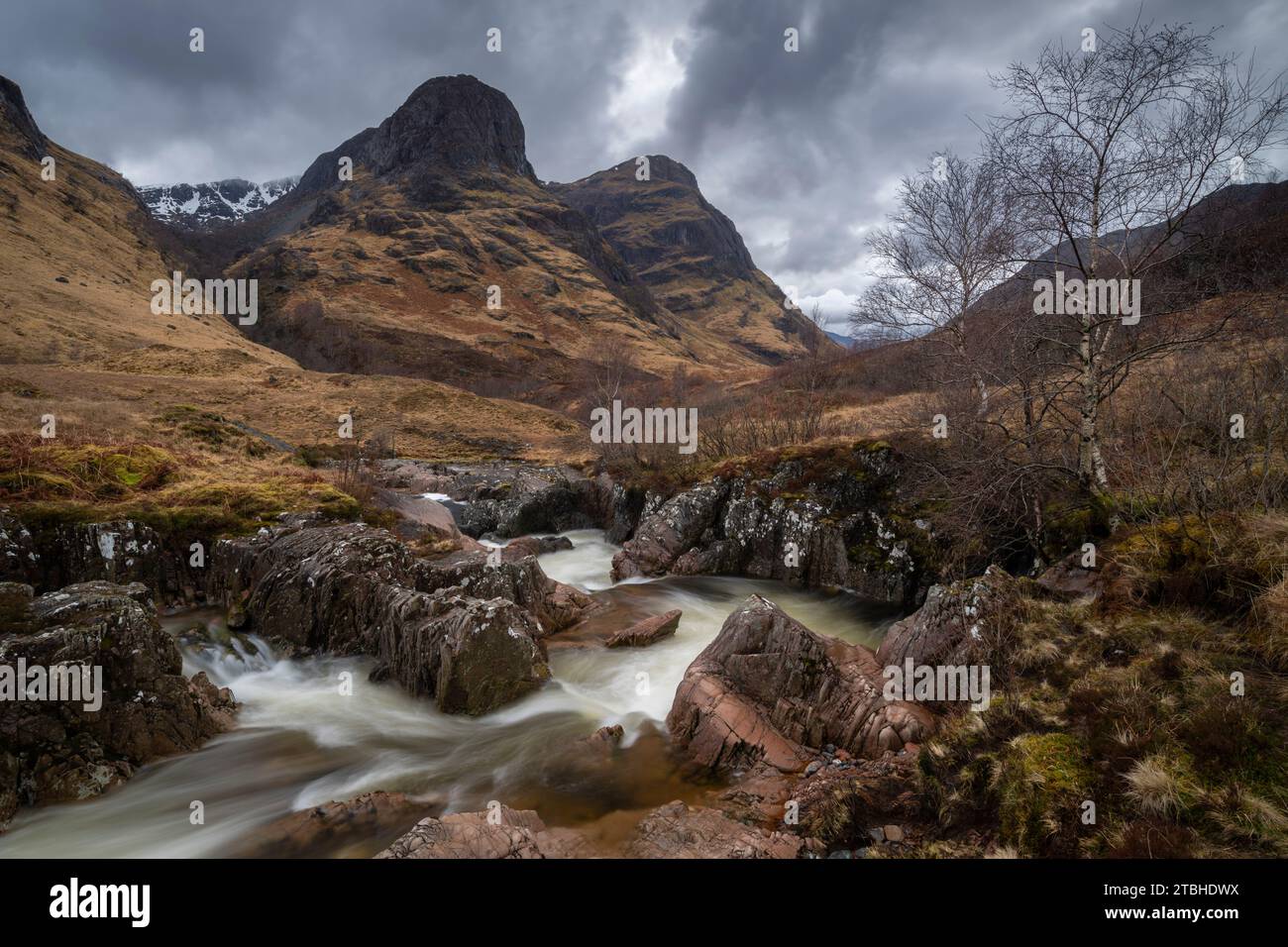 Il fiume Coe corre attraverso la valle di Glencoe sotto le montagne Three Sisters, Highlands, Scozia, Regno Unito. Primavera (marzo) 2023. Foto Stock