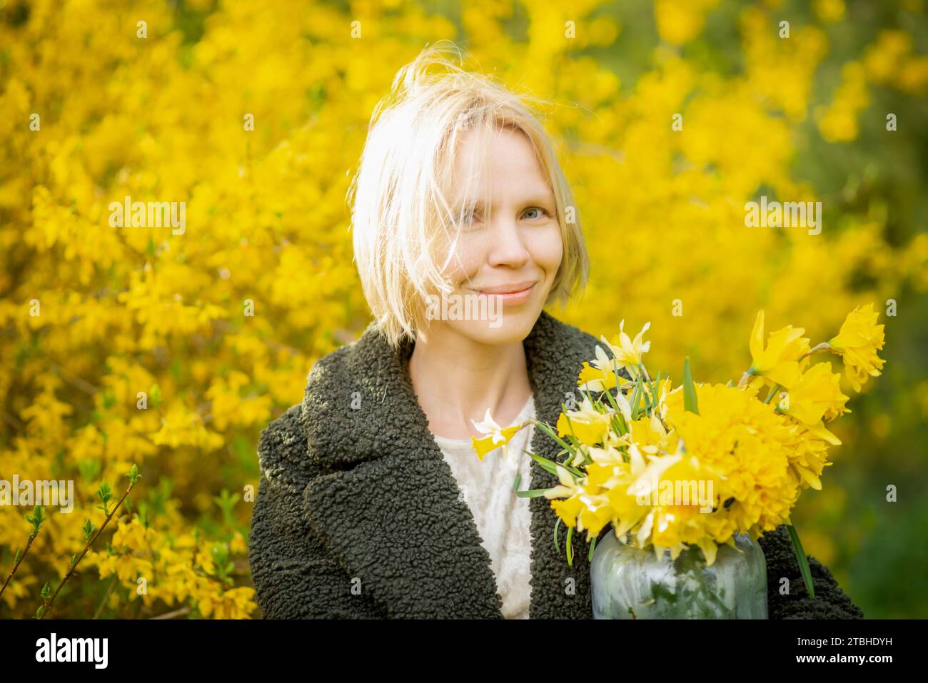 Donna su sfondo giallo con fiori gialli. Sorridente donna bionda di mezza età più di quaranta. Faccia felice, pensieri leggeri, sogni... Foto Stock