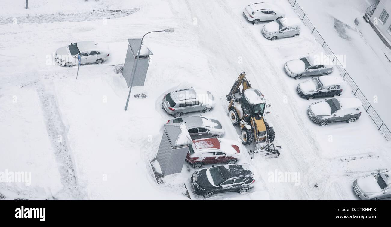 Il trattore pulisce le strade cittadine, rimuove neve e ghiaccio dopo forti nevicate e tormenta. Spazzaneve all'aperto, marciapiede pulito, vialetto stradale Foto Stock