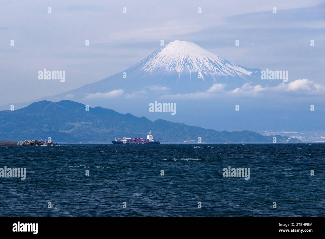 Questa funzione cattura la gloria e le dimensioni del Monte Fuji mentre incombe su una nave portacontainer che naviga verso il porto di Shimizu attraverso la baia di Suruga. Foto Stock