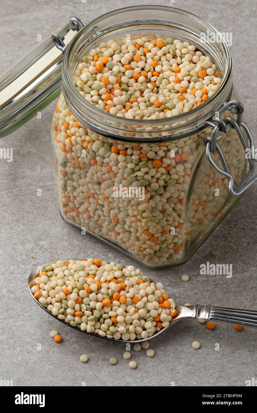 Vaso di vetro e cucchiaio con cumino tricolore di perle crude non cotte Foto Stock
