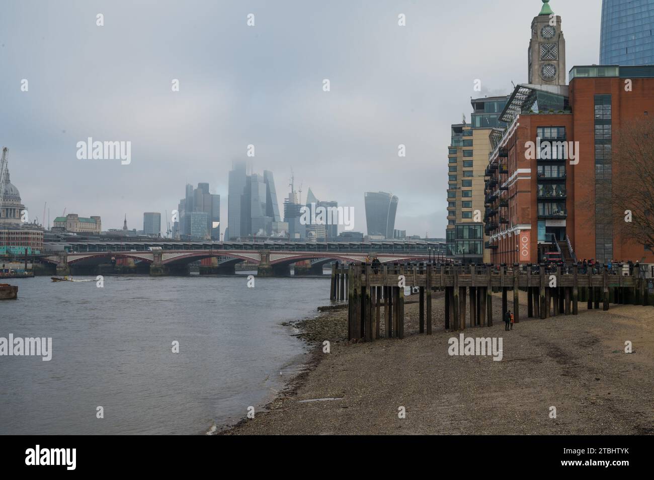 Skyline della città di Londra con grattacieli avvolti dalla nebbia in un giorno d'inverno. Persone che camminano accanto alla Oxo Tower sul molo Oxo Tower. South Bank, Londra, Regno Unito Foto Stock