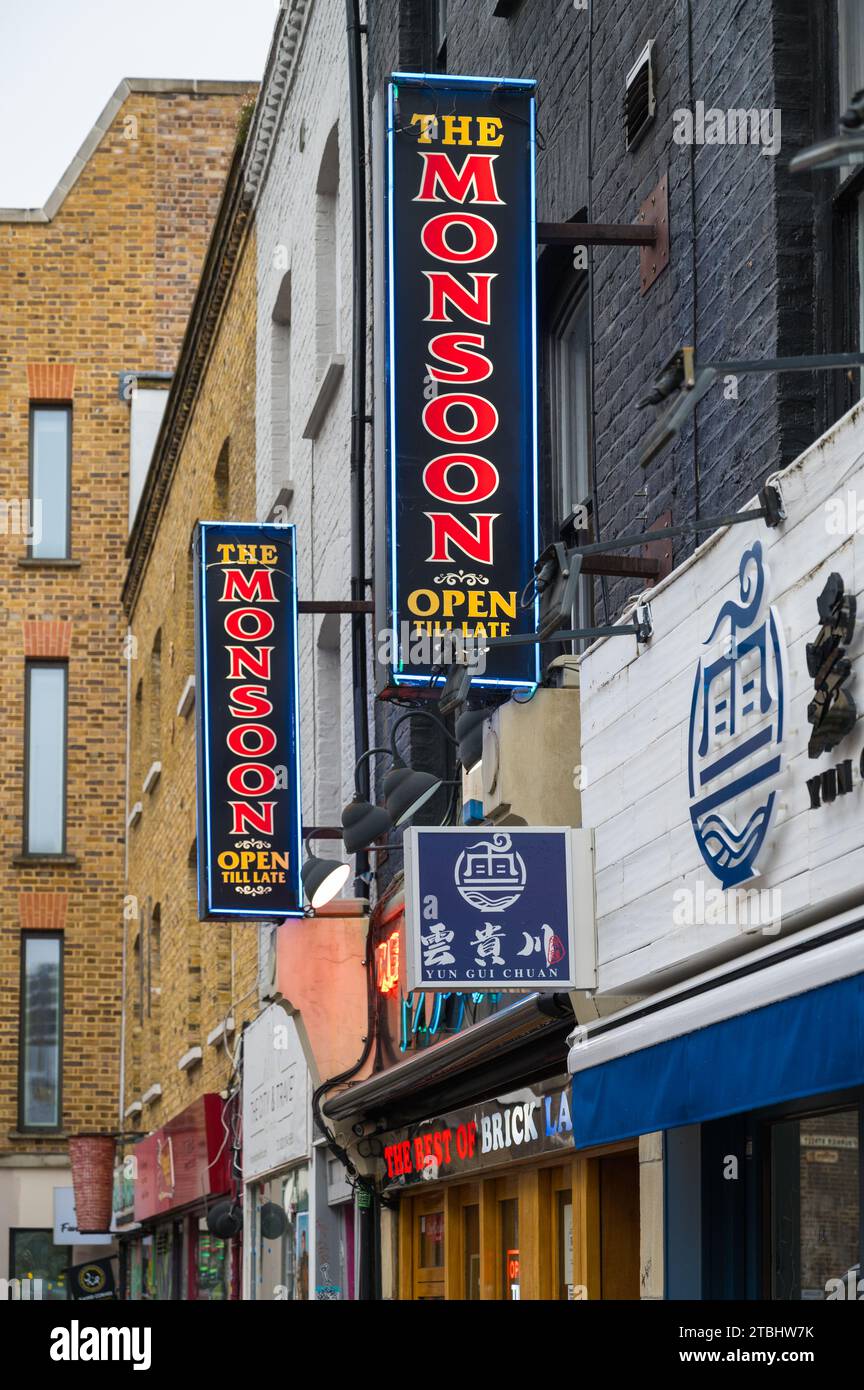 Coloratissimi cartelli illuminati sulla parete sopra l'entrata del ristorante indiano Monsoon e da asporto. Brick Lane, Londra, Inghilterra, Regno Unito Foto Stock