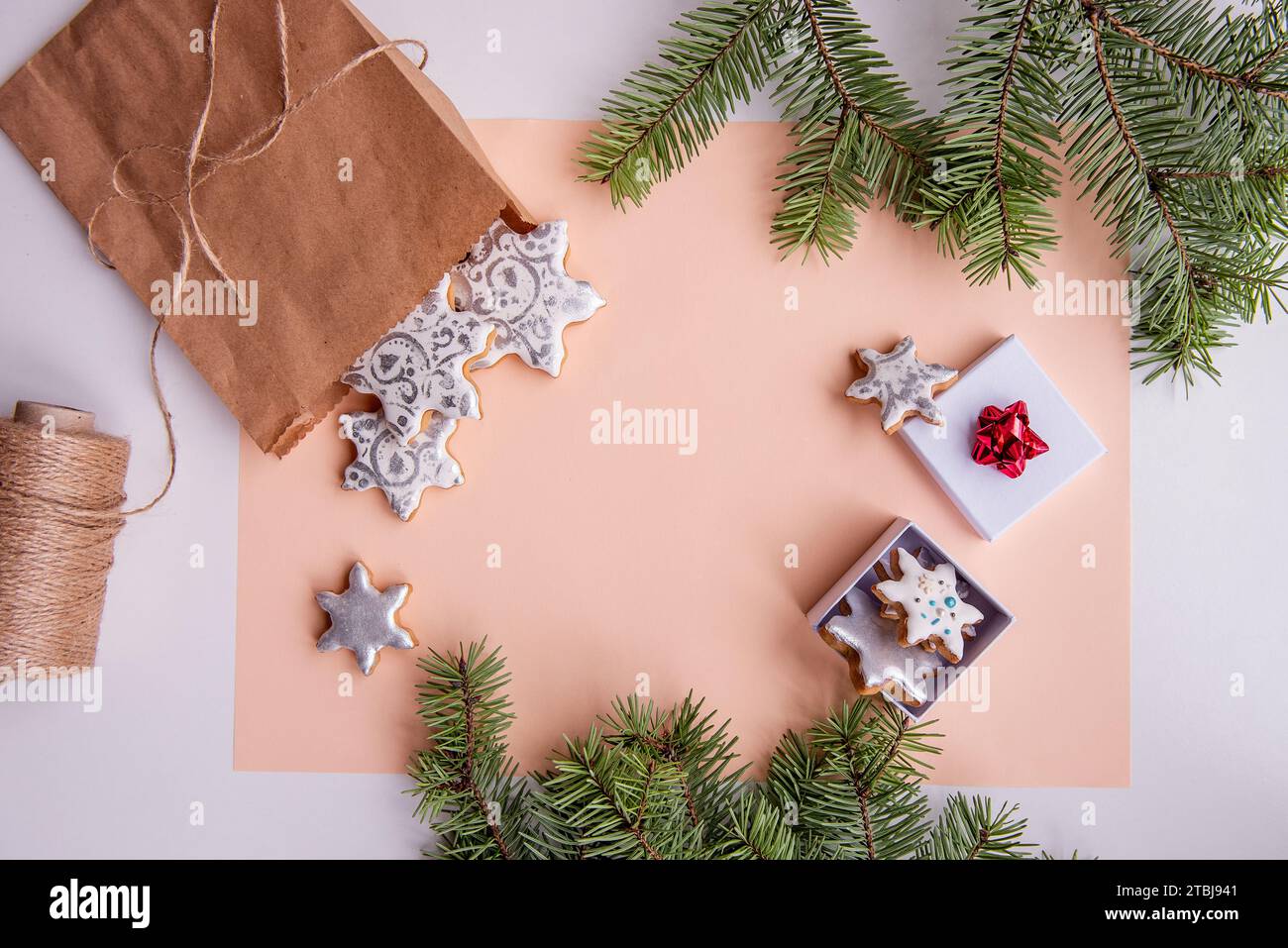 Sullo sfondo isolato di pesca si trova una borsa artigianale con biscotti al pan di zenzero argentato a forma di fiocco di neve per Natale. Vista dall'alto della natura morta con il verde Foto Stock