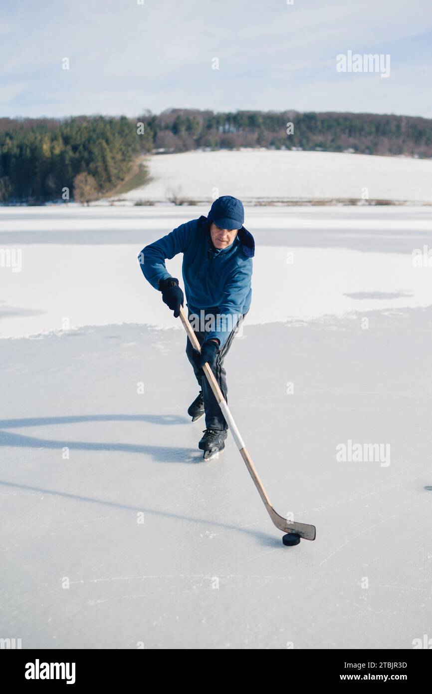 Uomo anziano sui pattini di ghiaccio con bastone da hockey sul lago ghiacciato in inverno. Concetto hobby degli anziani. Foto Stock