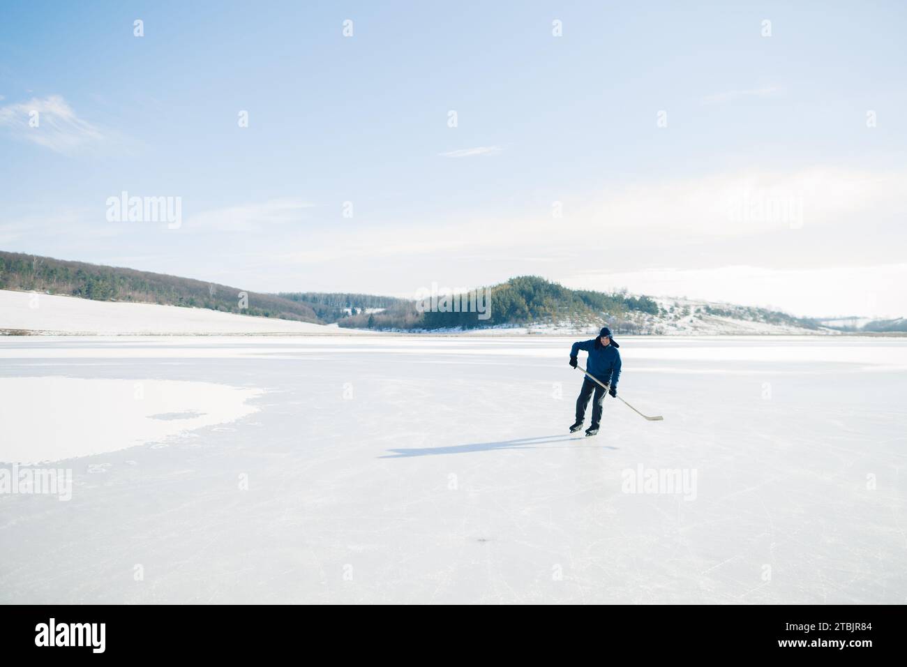 Uomo anziano sui pattini di ghiaccio con bastone da hockey sul lago ghiacciato in inverno. Concetto hobby degli anziani. Foto Stock