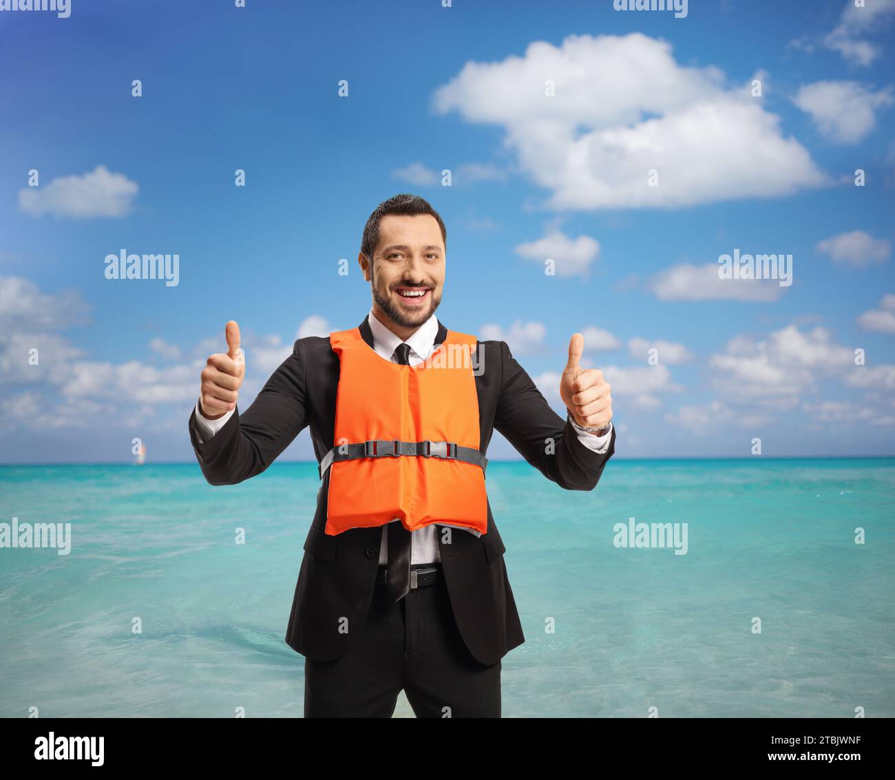 Uomo d'affari che indossa un giubbotto arancione e che mostra un cartello con il pollice in alto davanti a un mare Foto Stock