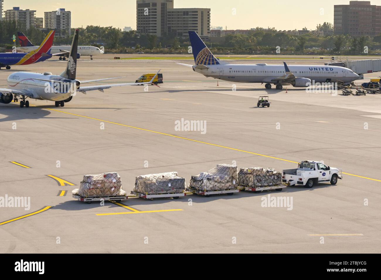 Miami, Florida, USA - 4 dicembre 2023: Rimorchi per il traino di camion con pallet cargo all'aeroporto internazionale di Miami Foto Stock