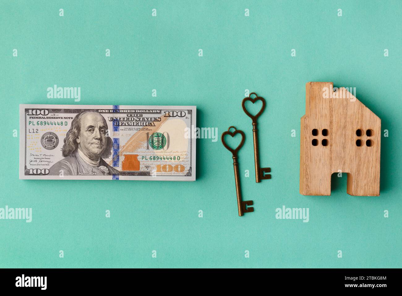 Modello di casa in legno, pila di dollari, chiavi di casa su sfondo verde. Il concetto di operazioni immobiliari, acquisto, affitto, assicurazione casa Foto Stock