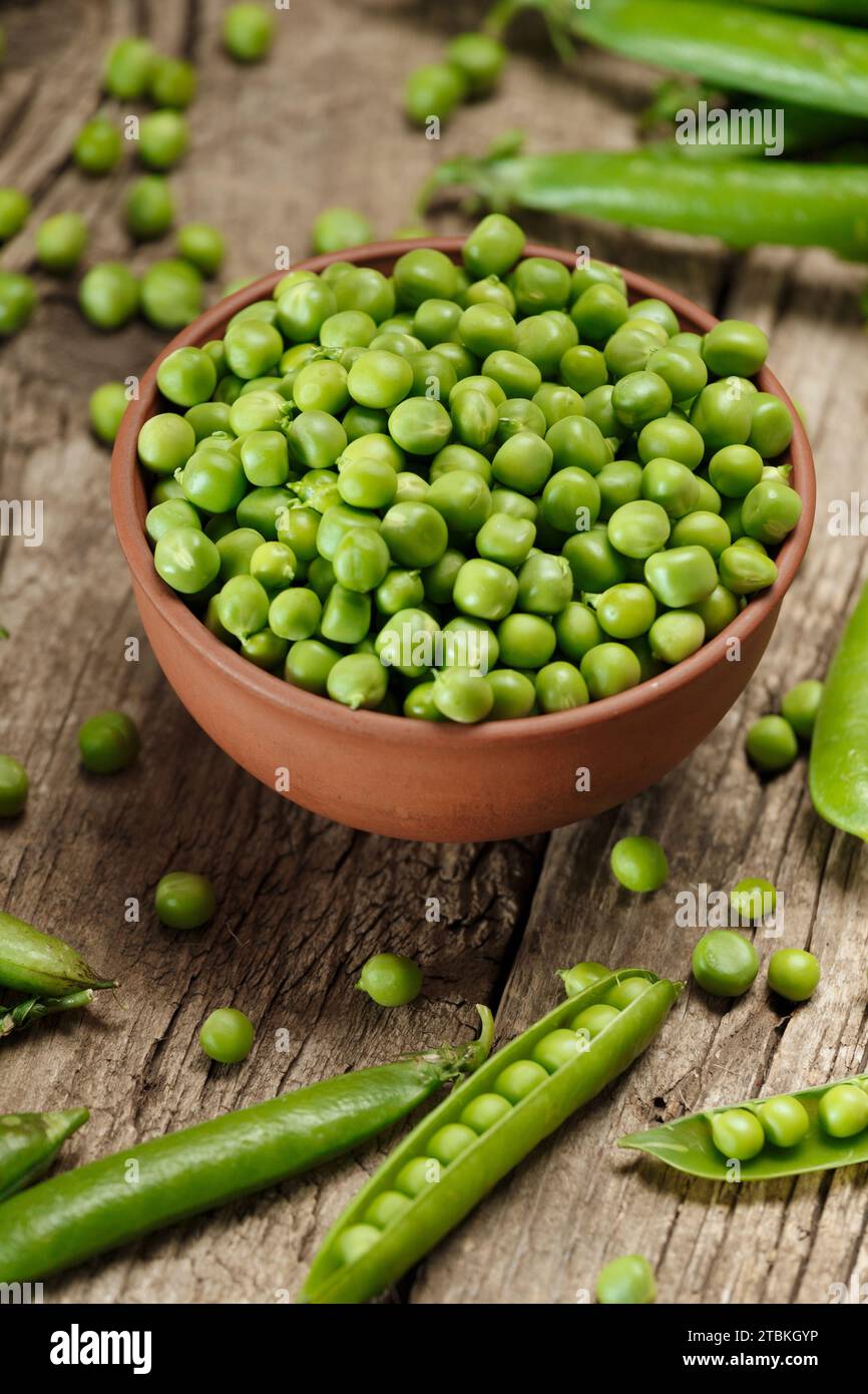 Piselli verdi biologici freschi in cialde chiuse e aperte, semi di piselli sparsi, piselli verdi sgusciati in una ciotola di argilla su uno sfondo di legno invecchiato. verdure Foto Stock