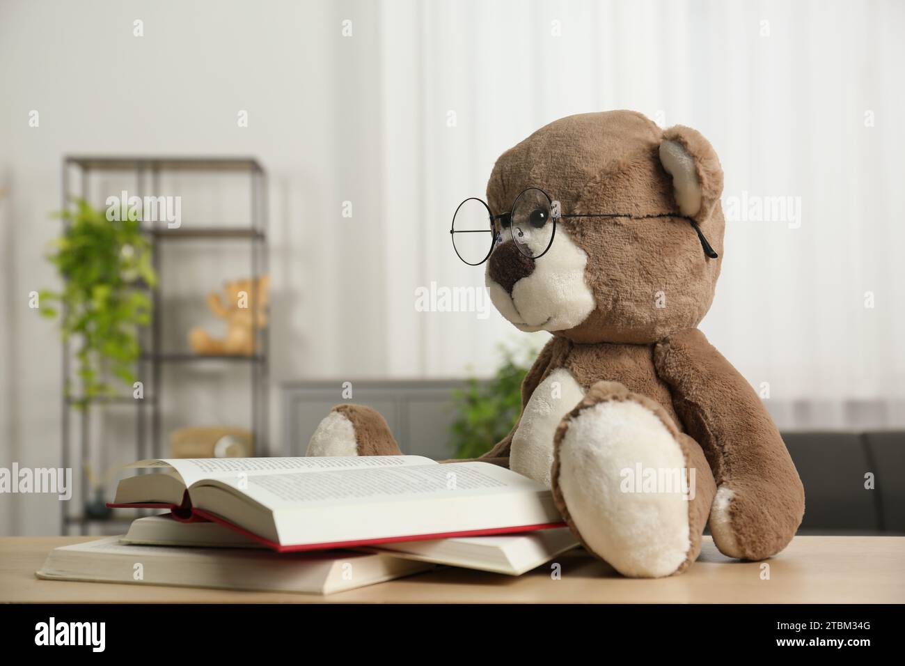 Orsacchiotto con occhiali e libri aperti su un tavolo di legno in camera Foto Stock
