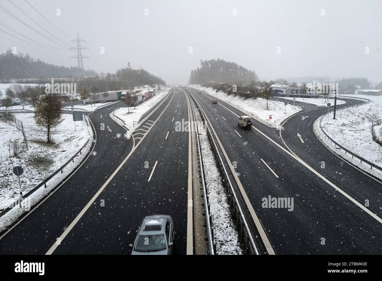 Le auto viaggiano sotto un ponte pedonale in inverno poiché la neve causa condizioni difficili di viaggio. Coburg, Germania Foto Stock
