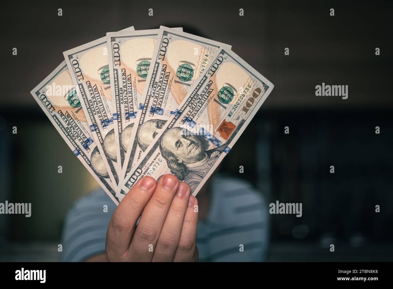 Mani che tengono contanti del dollaro. 1000 dollari in 100 fatture in primo piano di una mano dell'uomo su uno sfondo scuro. Foto Stock