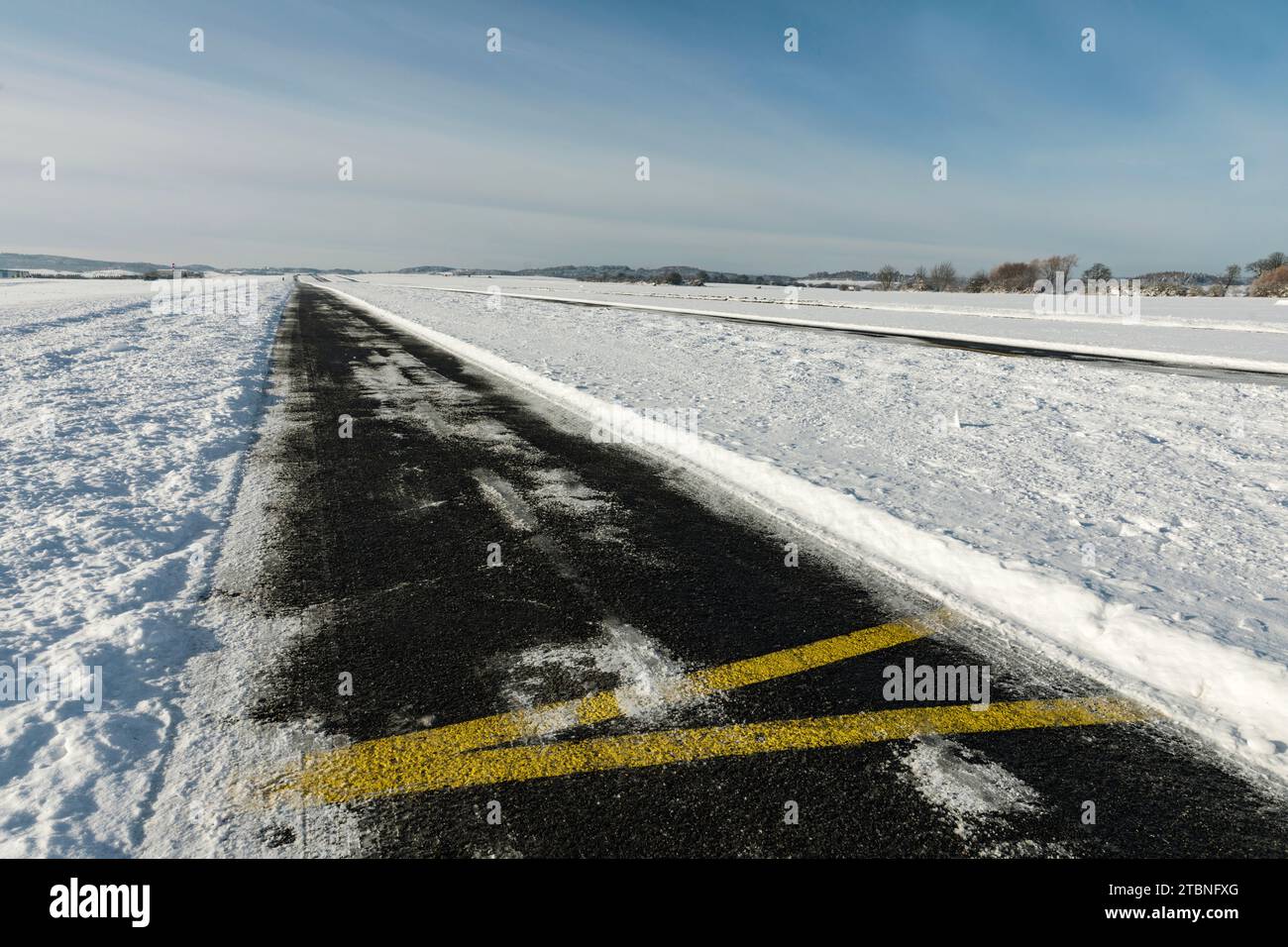 Una pista di rullaggio innevata in un piccolo aeroporto locale in una soleggiata giornata invernale. Foto Stock