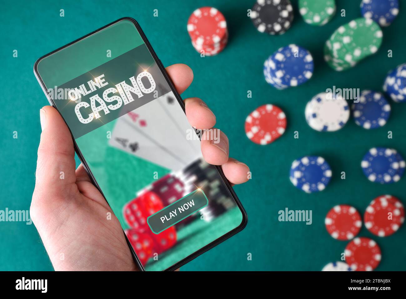 Mano con lo smartphone che mostra lo schermo con l'app di gioco del casinò online e le scommesse sui chip sul tavolo da gioco con sfondo verde feltro. Vista dall'alto. Foto Stock