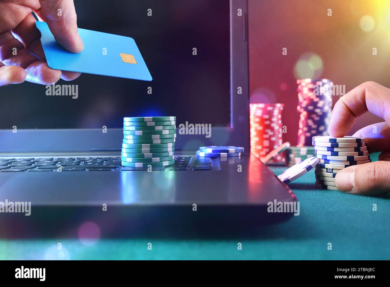 Giocatore di casinò che accede a una carta di pagamento per fare scommesse virtuali utilizzando un computer portatile. Con chip in una mano e carta di credito nell'altra. Vista frontale. Foto Stock