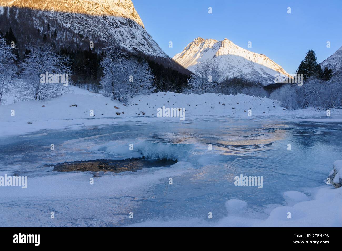 Un fiume ghiacciato con neve e montagne sullo sfondo e luce solare riflessa sul ghiaccio Foto Stock