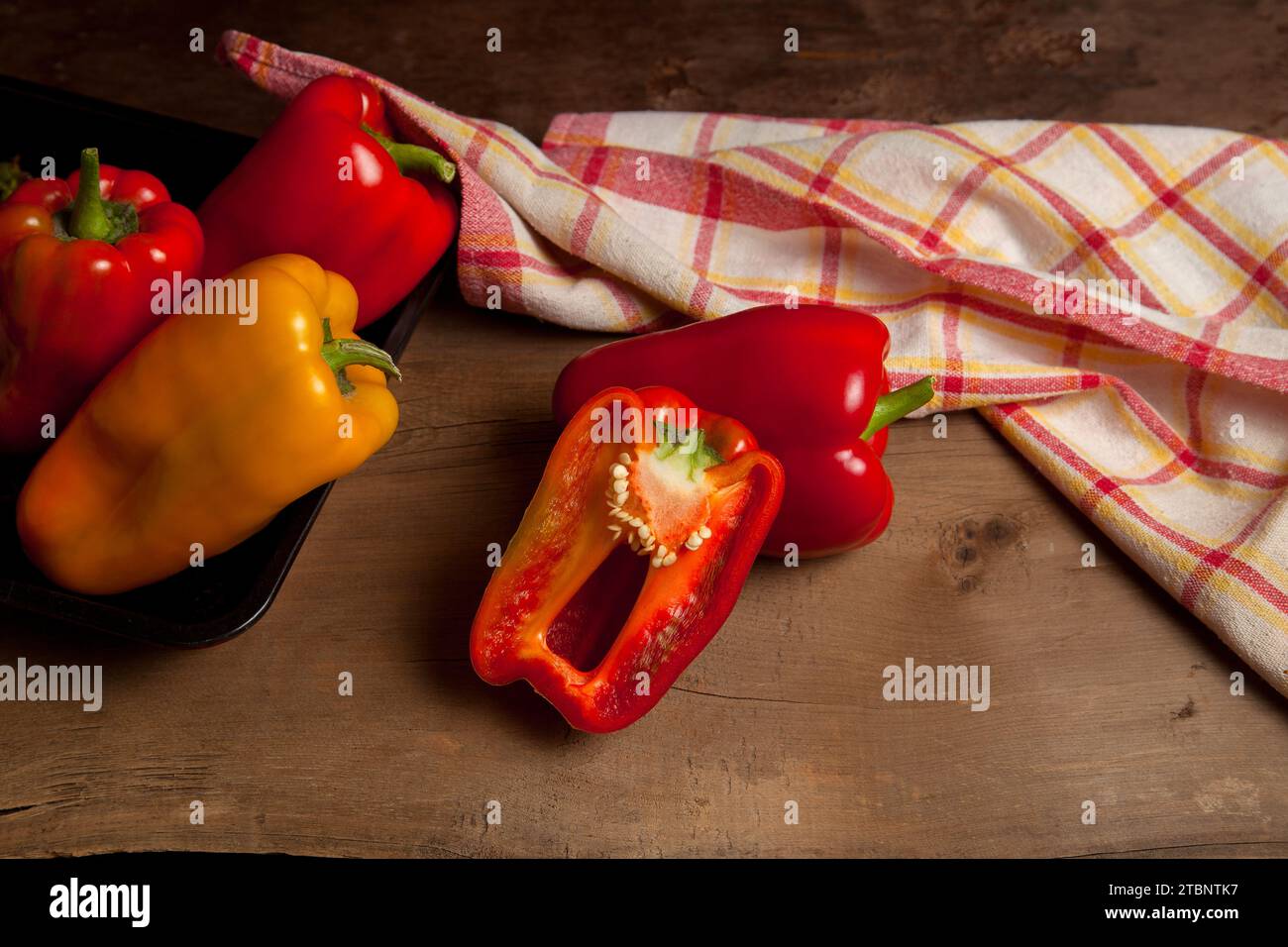Peperone rosso e giallo intero e mezzo (capsicum) conosciuto come peperone dolce, paprika su fondo di legno vintage con asciugamano da cucina rosso. Foto Stock