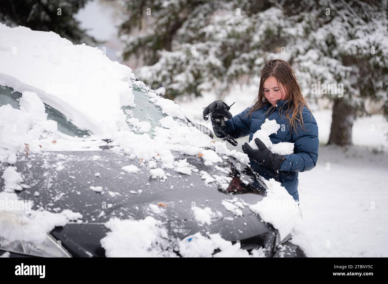 Ragazzo che fa palle di neve vicino a un'auto nera nevosa in inverno Foto Stock