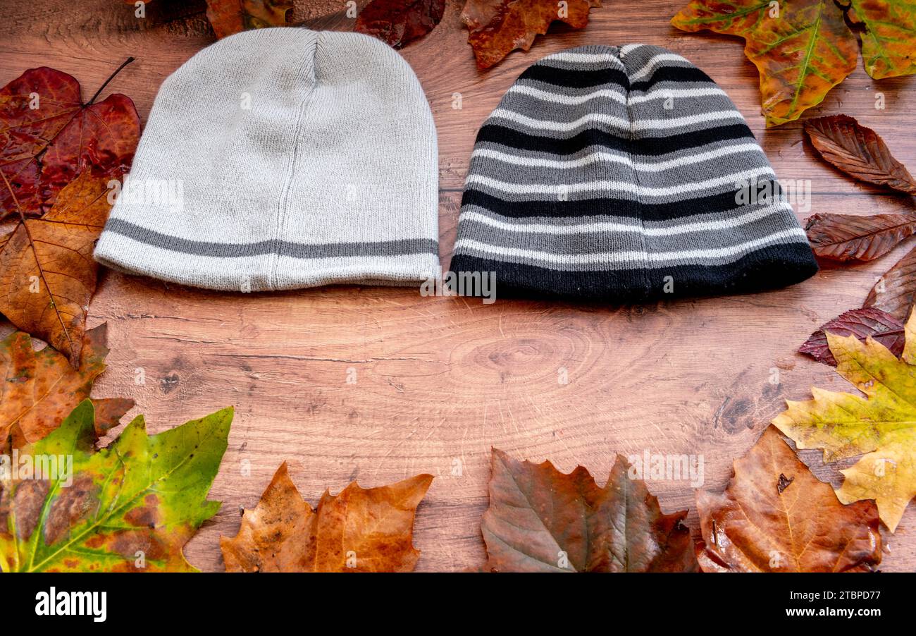 Cappelli di lana, cappelli di lana con un cerchio di foglie cadute su uno sfondo di legno. Foto Stock