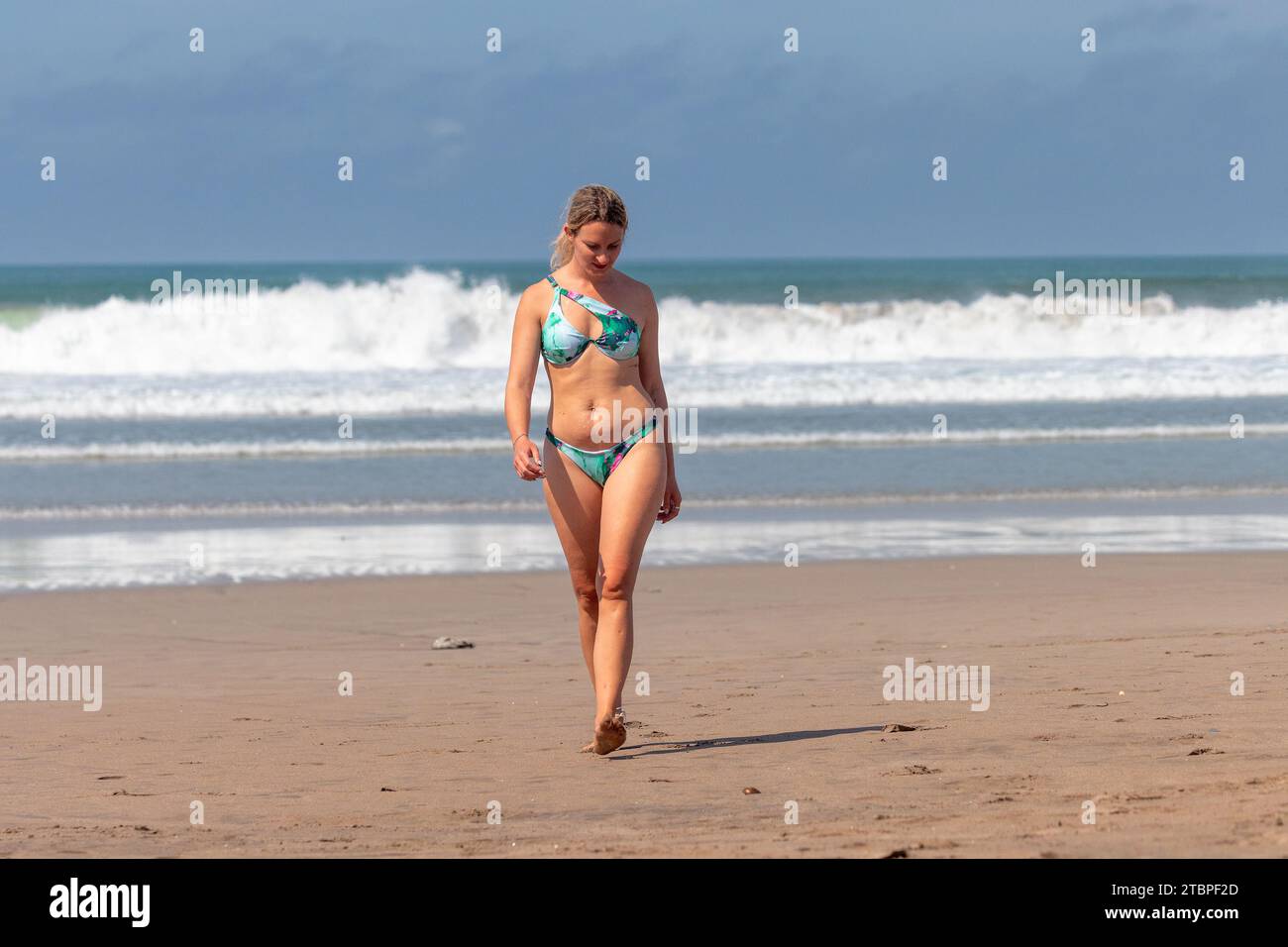 Una giovane donna sta camminando sulla spiaggia con grandi onde, Seminyak, Bali Island, Indonesia Foto Stock