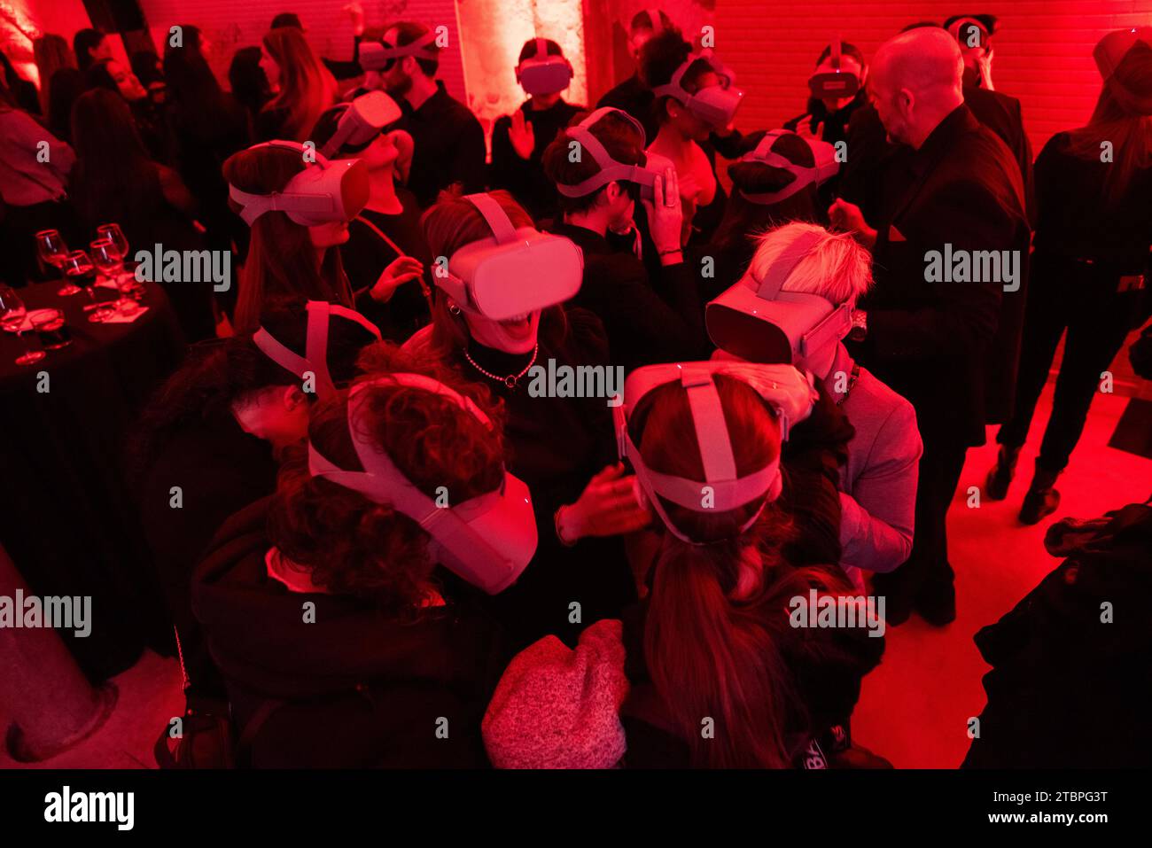 Le vivaci sfumature rosse avvolgono un evento mentre le persone indossano occhiali per realtà virtuale, trasportando le menti in regni invisibili in un'atmosfera futuristica di digitale condiviso Foto Stock