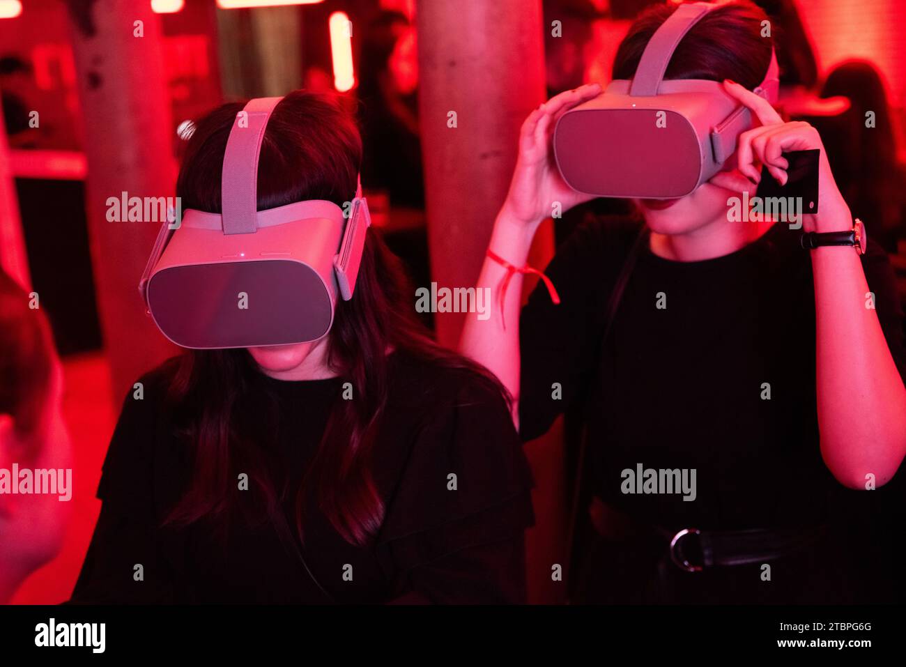 Due donne in un'immersione a luce rossa che esplorano insieme mondi virtuali, nell'energia dinamica di un evento tecnologico all'avanguardia Foto Stock