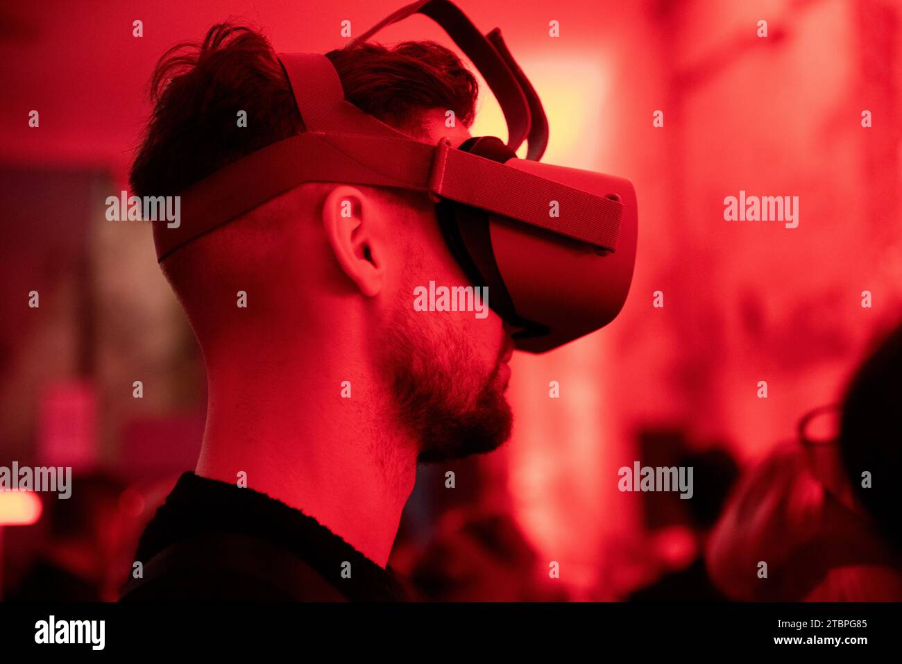 Nel bagliore cremisi, un uomo racconta il suo viaggio virtuale, navigando in regni invisibili attraverso gli occhiali VR in un evento tecnologico all'avanguardia. Foto Stock