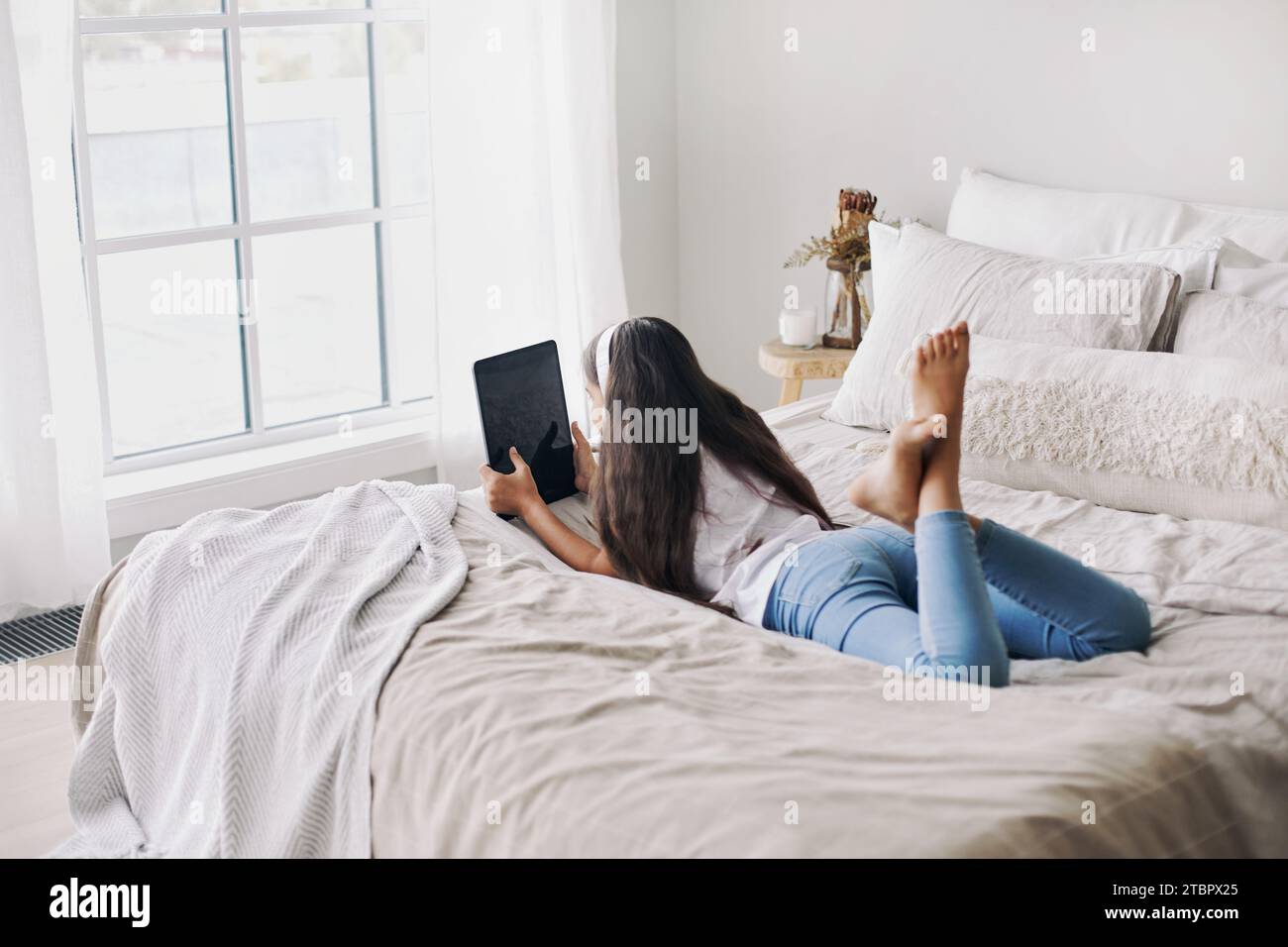 Adorabile ragazza di 12 anni preadolescente con cuffie wireless sdraiate sul letto con un tablet digitale. Giovani generazioni e abuso di tecnologia moderna, uso di gadget per Foto Stock