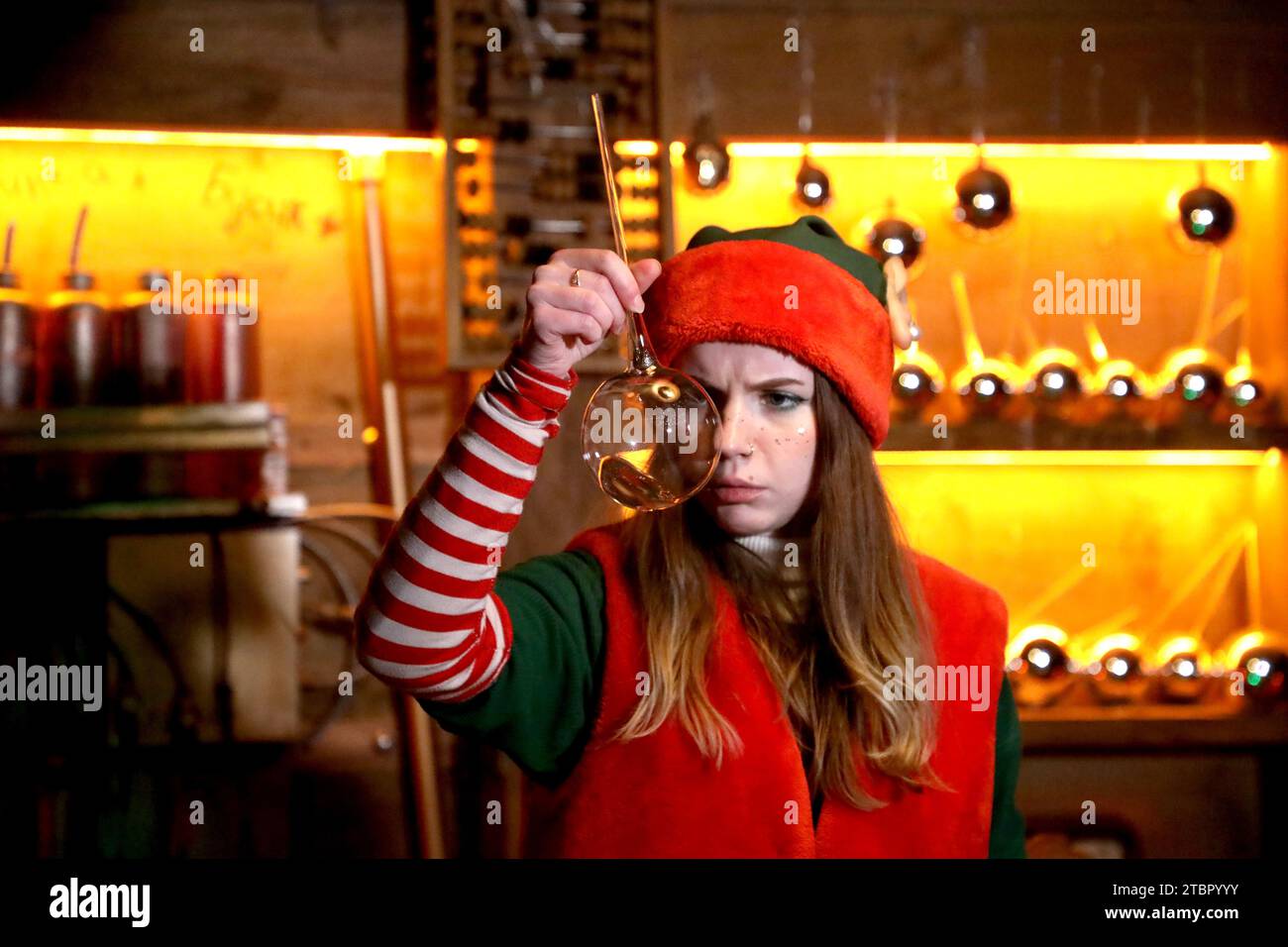 KIEV, UCRAINA - 7 DICEMBRE 2023 - un'attrice vestita come un elfo di Natale sembra stravagante in un pallone da laboratorio a fondo sferico mentre ruba un liquido Foto Stock